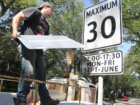 Ryan Laurin with the City of Winnipeg's Traffic Services division removes a cover from a school zone speed limit sign near Dorchester School in Crescentwood last week. (Kevin King/Winnipeg Sun file photo)