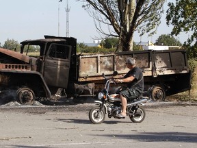 A local man rides a motorcycle past a truck burned by recent shelling on the outskirts of the southern coastal town of Mariupol September 7, 2014. REUTERS/Vasily Fedosenko
