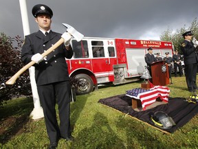 Belleville, Ont. firefighters Kyle Christopher, left, and Steve Morgan, right, stand by a piece of rusted, burned, scarred steel from the World Trade Centre on display alongside a fire bell and a pair of fire helmets as their colleague Steven Cowey, centre, speaks during a 9/11 memorial service at Station 1 on Moira Street West Thursday, Sept. 11, 2014. - JEROME LESSARD/THE INTELLIGENCER/QMI AGENCY