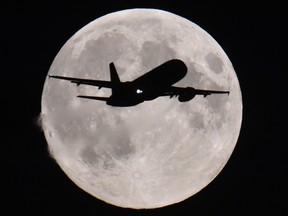 A passenger aircraft descends towards Heathrow Airport with a full moon seen behind, in west London, September 8, 2014. (REUTERS/Toby Melville)