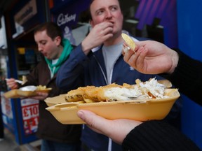 Customers eat their takeaway fish and chips outside the Wembley Bay fish and chip shop in west London, England. Deep-fried fish in a crispy batter with fat golden chips is still as popular as ever with the British public, ranked alongside roast beef, Yorkshire pudding and chicken tikka masala as the nation's favourite dish.  (Reuters)