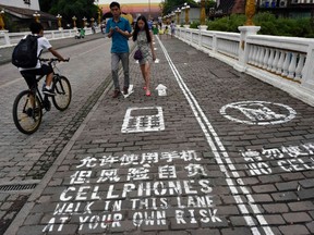 A man rides his bicycle as people walk on the "first mobile phone sidewalk in China", which was recently installed at a tourism area in Chongqing municipality, September 13, 2014. The mobile phone sidewalk in Chongqing was divided into two sides -- one was written with "Cellphones walk in this lane at your own risk" while the other with "No cellphones," as an attempt to reduce pedestrian incidents, local media reported. Picture taken September 13, 2014. REUTERS/China Daily