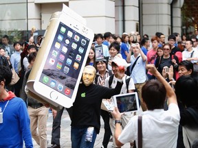 A man wearing a mask depicting Apple's co-founder Steve Jobs holds up a cardboard cut-out of Apple's new iPhone 6, as he walks into the Apple Store at Tokyo's Omotesando shopping district Sept. 19, 2014. REUTERS/Yuya Shino