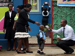 A school official takes a pupil's temperature using an infrared digital laser thermometer in front of the school premises, at the resumption of private schools, in Lagos on September 22, 2014. (REUTERS/Akintunde Akinleye)