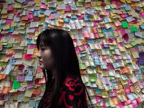 TOPSHOTSA woman walks past a wall of post it messages of support near an occupied area in Hong Kong on October 7, 2014.  Small knots of pro-democracy demonstrators remained on Hong Kong's streets after protest leaders agreed to talks with the government and dwindling demonstrator numbers dropped further.  AFP PHOTO / Philippe Lopez