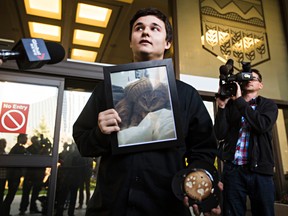 Derek North holds a picture of his cat Pudge, as well as a framed paw print, outside court Tuesday after a sentencing hearing for Zachary McKinnon, who has admitted killing the cat and cutting it up to cook it in Edmonton, Alta., on Tuesday, Oct. 7, 2014. Codie McLachlan/Edmonton Sun