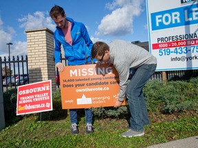 Martin Flanagan, Programs Coordinator for Emerging Leaders, left, and Ryan Cole, Cultural Initiatives Coordinator for Emerging Leaders, place a sign in the ground along Richmond Street at Horton Street promoting their website, ownthevote.ca, in London, Ontario on Wednesday October 8, 2014. (CRAIG GLOVER, The London Free Press)