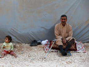A Kurdish refugee man and a baby from the Syrian town of Kobani sit beside a tent in a camp in the southeastern town of Suruc, Sanliurfa province October 10, 2014. The U.S. military conducted nine airstrikes against Islamic State militants in Syria during the past two days, including seven strikes near the border town of Kobani, U.S. Central Command said on Friday. REUTERS/Umit Bektas