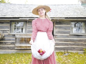 Alison Deplonty carries apples in her apron outside of the Elgie log cabin at Fanshawe Pioneer Village. (CRAIG GLOVER, The London Free Press)