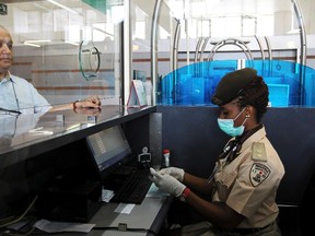 A female Immigration officer wearing a facemask and gloves checks a passenger's passport at the Nnamdi Azikiwe International Airport in Abuja, August 11, 2014. (REUTERS/Afolabi Sotunde)