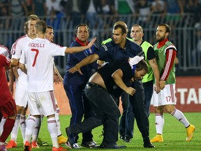 A policeman escorts a Serbian fan that invaded the pitch after a flag with Albanian national symbols was flown by a remotely operated drone during the UEFA Euro 2016 group I qualifying football match between Serbia and Albania in Belgrade on October 14, 2014. (AFP PHOTO / GENT SHKULLAKU)