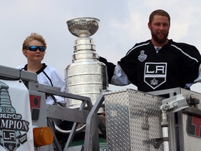 Kings defenceman Jake Muzzin (right) holds the Stanley Cup while riding a firetruck next to his cousin Luke Woudsma (left) during a parade in Woodstock, Ont. on July 27, 2014. Muzzin signed a contract extension with the kings on Oct. 15, 2014. (Greg Colgan/QMI Agency)