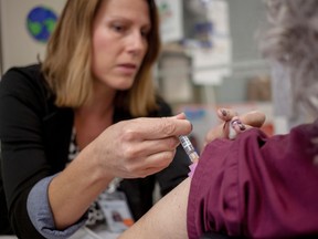 From left, Terry Brooks, a public health nurse, administers a flu-shot to Rhonda Fenner, a teacher at the Carlan Centre daycare in Whitecourt. on Oct. 7, 2014. Young children and those who work with them, considered to be at a higher risk of catching the flu were vaccinated a few weeks ahead of the annual blitz to vaccinate people. This year starting on Oct. 20 those living, working and studying in Alberta can go get the flu vaccination.