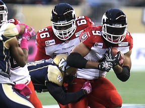 Calgary Stampeders RB Jon Cornish is hit by Winnipeg Blue Bomber DB Maurice Leggatt during CFL action at Investors Group Field in Winnipeg, Man., on Sat., Oct. 18, 2014. Kevin King/Winnipeg Sun/QMI Agency