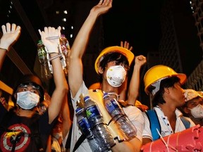 Pro-democracy protesters, protecting themselves with helmets, masks, foam pads and empty plastic bottles, raise their hands at riot police as a gesture of peace after they were told by visiting lawmakers not to charge the police defence line, at Mongkok shopping district in Hong Kong early October 20, 2014.   REUTERS/Liau Chung-ren