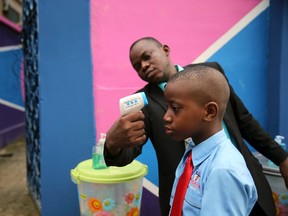 A school official takes a pupil's temperature using an infrared digital laser thermometer in front of the school premises, at the resumption of private schools, in Lagos in this Sept. 22, 2014 file photo. REUTERS/AKINTUNDE AKINLEYE