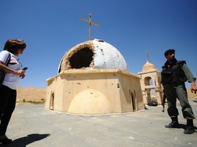 A woman and a soldier loyal to Syria's president Bashar Al-Assad stand beside a damaged church in Maaloula August 21, 2014. (REUTERS/Omar Sanadiki)