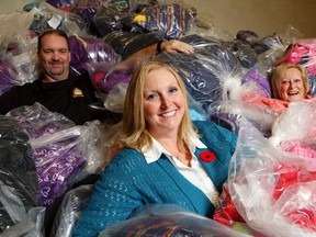 Adopt-a-Child chairwoman Const. Ann Earle of the Belleville Police Service sits in a pile of donated clothes with Stirling-Rawdon Police Const. Scott Burke and Adopt-a-Child volunteer Barb Lea at police headquarters Friday in Belleville. There's only one week remaining in the program but just half of its clothing goal has been reached, meaning donations are needed urgently.