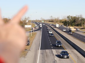 Bunny Morrison, the mother of a Canadian military corporal based in Ottawa, raises her hand in a peace sign as the hearse bearing the body of Cpl. Nathan Cirillo travels Highway 401 at Belleville, Ont. Friday, October 24, 2014. Hundreds of people lined overpasses above Canada's busiest highway to honour Cirillo. "I'm all for peace," said Morrison, who also wore red to support Canadian troops. (Luke Hendry, QMI Agency)