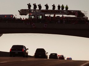 Firemen salute from the top of their truck as residents of Port Hope stand below them with flags on a bridge to honour Corporal Nathan Cirillo as the motorcade and hearse carrying his body passes along Highway 401, the nation's "Highway of Heroes", enroute to Hamilton, Ontario October 24, 2014. Police said a home-grown radical, Michael Zehaf-Bibeau, killed Cirillo, 24, on Wednesday before fleeing into the Parliament building where he was shot dead near where Canadian Prime Minister Stephen Harper was meeting with lawmakers.    REUTERS/Fred Thornhill