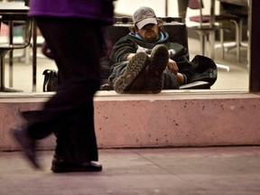 A man sleeps by the window of the Stanley Milner Library as pedestrians walk in Edmonton in this November 26, 2010 file photo. (CODIE MCLACHLAN/QMI AGENCY)