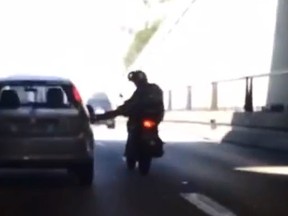 A motorcyclist attempting to kick the back of a car. 

(YouTube screenshot)