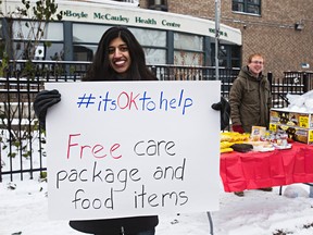 Dr. Shawna Pandya, left, holds up a sign as Rob Kingston mans the table outside the Boyle-McCauley Health Centre in Edmonton, Alta., on Sunday, Nov. 9, 2014. Dr. Shawna Pandya put together a food giveaway in reaction to news about a Florida man who was charged for feeding the homeless. Codie McLachlan/Edmonton Sun/QMI Agency