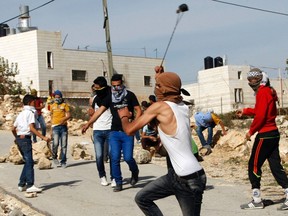 A Palestinian uses a slingshot to throw stones toward Israeli soldiers during clashes in Siear town near the West Bank city of Hebron November 11, 2014. (REUTERS/ Mussa Qawasma)