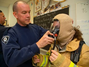 London firefighter James Bell helps student volunteer Jennifer Eid, 15 of Saint Andre Bessette Catholic Secondary School into their bunker gear including breathing apparatus during a Health Technology class at the school in London, Ont. on Monday November 10, 2014. 
Mike Hensen/The London Free Press/QMI Agency