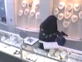A burka-wearing thief holds a gun as he places jewelry in a bag. (Toronto Police handout)