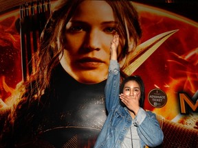 Student Natchacha Kongudom flashes a three-finger salute inspired by the movie "The Hunger Games" in front of a billboard of the film outside the Siam Paragon cinema in Bangkok November 20, 2014. Three Thai university students were taken into police custody on Thursday for handing out free tickets to the latest film in the Hunger Games series, from which Thai protesters have borrowed a gesture of resistance to a totalitarian government. The salute has become emblematic with Thai pro-democracy protesters, and the Thai government has warned the public against using it.  REUTERS/Chaiwat Subprasom