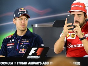 Red Bull Racing's Sebastian Vettel (left) watches Ferrari's Fernando Alonso record footage on his phone during the press conference in Abu Dhabi on November 20, 2014 ahead of the Abu Dhabi Formula One Grand Prix. (AFP PHOTO/TOM GANDOLFINI)