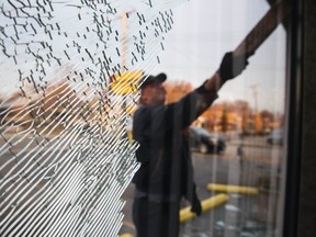 John Adams uses a board to clean broken glass out of window panes at his friends vandalized business following a second night of protests in Ferguson, Missouri November 26, 2014. Aiming to head off new looting and rioting, Missouri's governor on Tuesday ordered National Guard reinforcements into the St. Louissuburb of Ferguson following overnight violence ignited by the clearing of a white police officer in the fatal shooting of an unarmed black teenager. REUTERS/Lucas Jackson (UNITED STATES - Tags: CIVIL UNREST CRIME LAW)