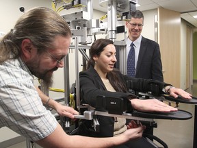 PhD student Noor Aldahhan plays the role of a patient as technician Justin Peterson, left, sets up the Kinarm, a robotic device that measures arm movements, while Dr. James Reynolds, right, looks on during Wednesday's official opening of the Queen's University Centre for Neuroscience Studies at Hotel Dieu Hospital. (Michael Lea/The Whig-Standard)