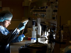 PhD student Aaron Johnson uses a pipette to transfer samples while wearing garb that will be used to protect researchers in a new HIV/AIDS research facility at Western University. (CRAIG GLOVER, The London Free Press)