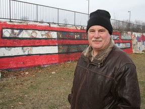 David Dossett stands in front of the now-vandalized mural he created on a retaining wall during last summer's On the Wall street art festival. It was covered in red paint, as were a couple of others. (Michael Lea/The Whig-Standard)