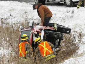 This motorist gives a hand to Quinte West, Ont. firefighters so they can open the hood of his pickup truck after it wound up in a ditch along Moira Street West, near Wallbridge-Loyalist Road, late Thursday morning, Dec. 11, 2014. - JEROME LESSARD/THE INTELLIGENCER/QMI QGENCY