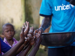 A social mobilizer from NGO Association des Jeunes Conditionnaires et Manutentionnaires (AJCOM), a UNICEF partner, carries a basin of water past the soapy hands of children, to help prevent the spread Ebola in Conakry, Guinea, in this handout photo provided by UNICEF. (Timothy La Rose/Reuters)