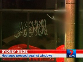 A black flag with white Arabic writing is held up at the window of the Lindt cafe, where hostages are being held, in this still image taken from video from Australia's Seven Network on December 15, 2014. Dozens of hostages were trapped inside the central Sydney cafe on Monday, with local television showing some being forced to hold up a black flag with white Arabic writing in the window, raising fears of an attack linked to Islamic militants. REUTERS/Reuters TV via Seven Network/Courtesy Seven Network