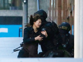 A hostage runs towards a police officer outside Lindt cafe, where other hostages are being held, in Martin Place in central Sydney December 15, 2014. Two more hostages have run out of the cafe at the center of a siege in Sydney, Australia's largest city, according to a Reuters witness at the site. The two women were both wearing aprons indicating they were staff at the Lindt cafe where a gunman has been holding an unknown number of hostages for several hours. Three men had earlier run out of the cafe.  REUTERS/Jason Reed