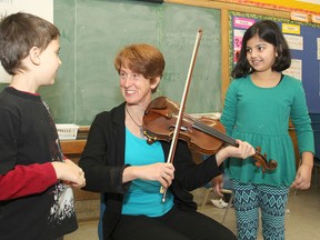Karma Tomm, director of the Queen's Conservatory of Music and proponent of a new, free, after-school music instruction program, demonstrates her violin to First Avenue Public School students Andrew Tugwood, left, and Suchi Patel in Kingston. (Michael Lea/The Whig-Standard)