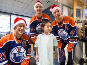 Ellia Ito-Nakao gets her photo taken with Edmonton Oilers defenceman Andrew Ference (left), forward David Perron (centre), and forward Taylor Hall, who visited the Stollery Children's Hospital in Edmonton on Monday, Dec. 22, 2014. The four players bought Christmas gifts for kids and delivered presents. (IAN KUCERAK/Edmonton Sun)