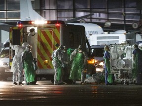 A healthcare worker (C) who was diagnosed with Ebola after returning from Sierra Leone is walked from an ambulance and put into a quarantine tent trolley before being wheeled into a Hercules Transport plane at Glasgow International Airport on December 30, 2014, bound for The Royal Free hospital in London.  AFP PHOTO / STR