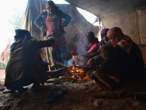 Displaced Syrians warm themselves around a fire inside a tent during a winter storm in Jabal al-Zawiya in the southern countryside of Idlib. REUTERS/Stringer