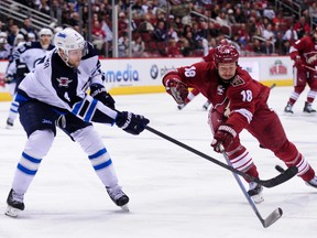 Jan 8, 2015; Glendale, AZ, USA; Winnipeg Jets defenseman Paul Postma (4) defends as Arizona Coyotes right wing David Moss (18) grabs for the puck during the second period at Gila River Arena. Mandatory Credit: Matt Kartozian-USA TODAY Sports