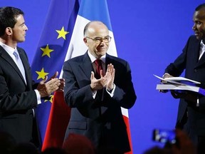 French Prime Minister Manuel Valls (L) and Interior Minister Bernard Cazeneuve (C) applaud as Lassana Bathily (R), 24, holds his citizenship papers during a ceremony at the Interior Ministry in Paris January 20, 2015.   REUTERS/Charles Platiau