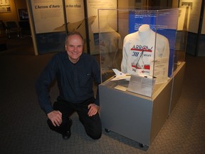 Elgin County Museum curator Mike Baker crouches next to a display case containing a model of the Avro Arrow and other artifacts. The museum is set to open an exhibit about the Arrow in early February.