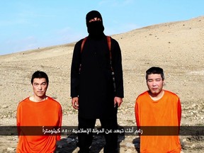 An image grab taken off a video on January 20, 2015, reportedly released by the Islamic State (IS) group through Al-Furqan Media, one of the Jihadist platforms used by the militant organisation on the web, allegedly shows Japanese hostages Kenji Goto (L) and Haruna Yukawa (R) in orange jumpsuits with a black-clad militant brandishing a knife as he addresses the camera in English, standing between them at an undisclosed location.  AFP PHOTO / HO / AL-FURQAN MEDIA