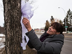 Debbie Raymond places a white bow on a tree along Poirier Avenue in St. Albert, Alta., on Friday, Jan. 23, 2015. Raymond and Tara McCormick started United in Light St. Albert, and have placed thousands of bows around the city since last week's shooting of two RCMP officers. Cst. David Wynn and auxiliary officer Cst. Derek Bond were shot last week while investigating a stolen truck at a casino in St. Albert. Bond was later released from hospital but Wynn succumbed to his injuries and passed away on Wednesday. Wynn's RCMP regimental funeral will be held Monday, Jan. 26, at 2 p.m. at Servus Place, 400 Campbell Road in St. Albert. Codie McLachlan/Edmonton Sun/QMI Agency