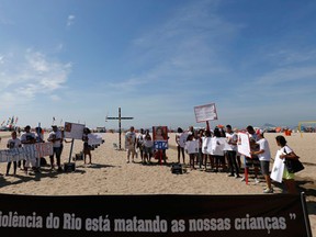 Demonstrators protest next to a cross fixed by NGO Rio de Paz (Peace Rio), in memory of children who died in recent violence, on Copacabana beach in Rio de Janeiro. The banner in front reads, "Violence in Rio is killing our children."  (REUTERS/Sergio Moraes)